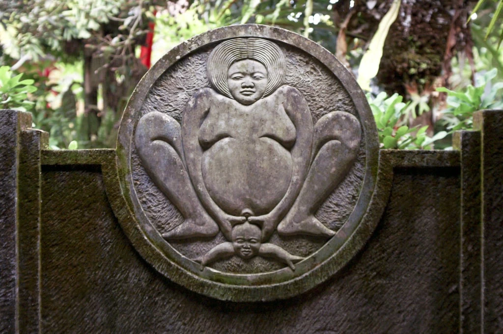 A circular stone relief showing a large female figure and a smaller child figure below, with greenery in the background.